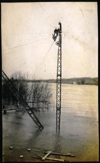 Photo of a recent flood, early 20th century, with two men sitting on top of a crane to escape the water